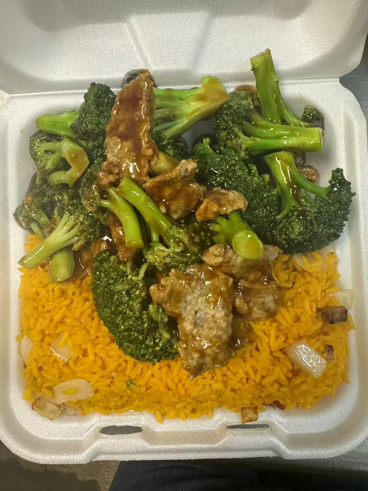 Beef and broccoli in brown sauce over yellow rice in a takeout box