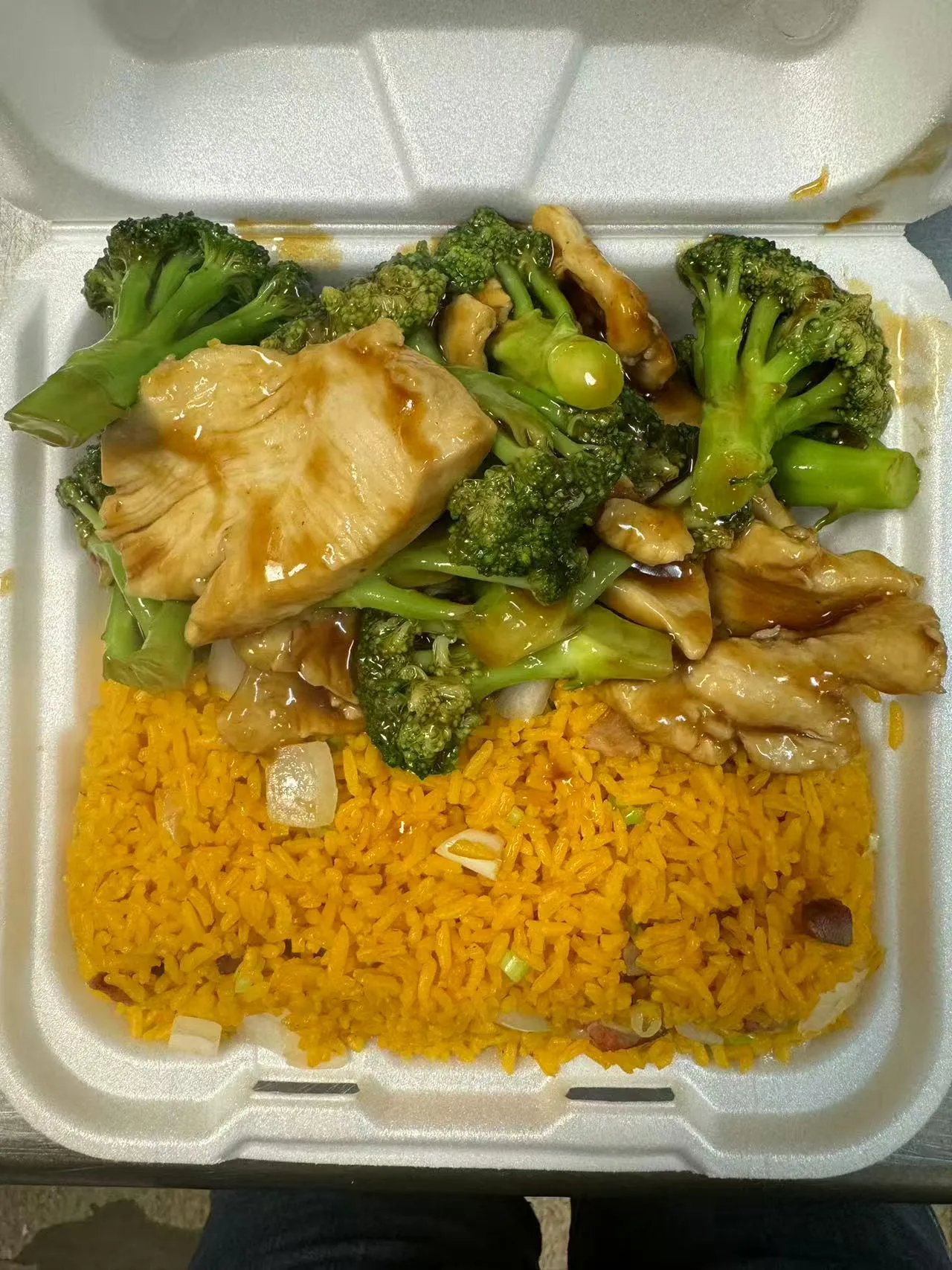 Chicken and broccoli with brown sauce over yellow rice in a takeout box