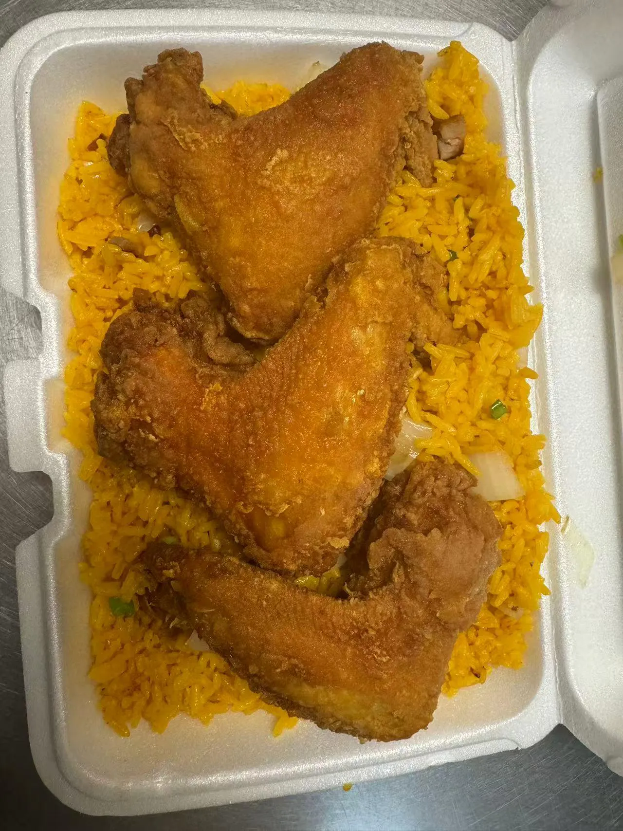Crispy fried chicken wings over yellow rice in a takeout box