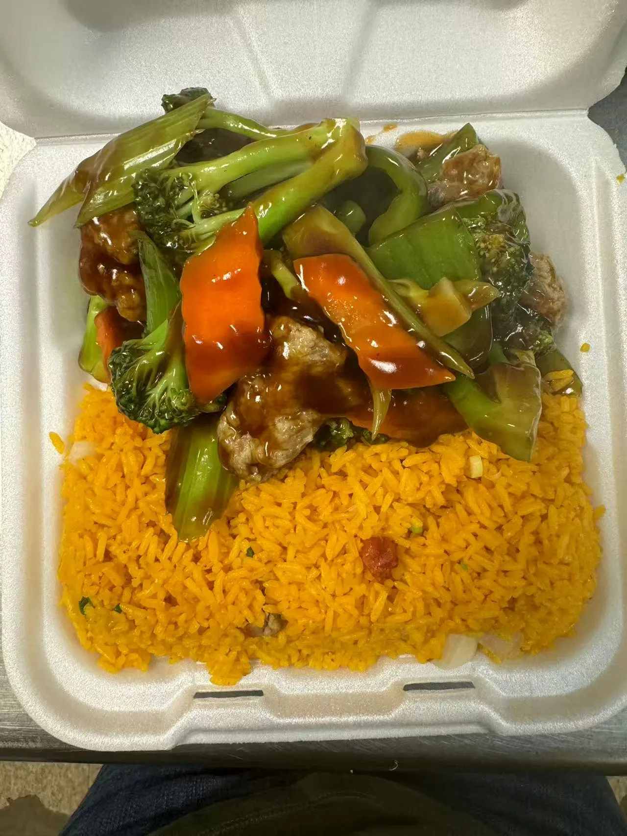 Mixed vegetable and meat stir-fry over yellow rice in a takeout box