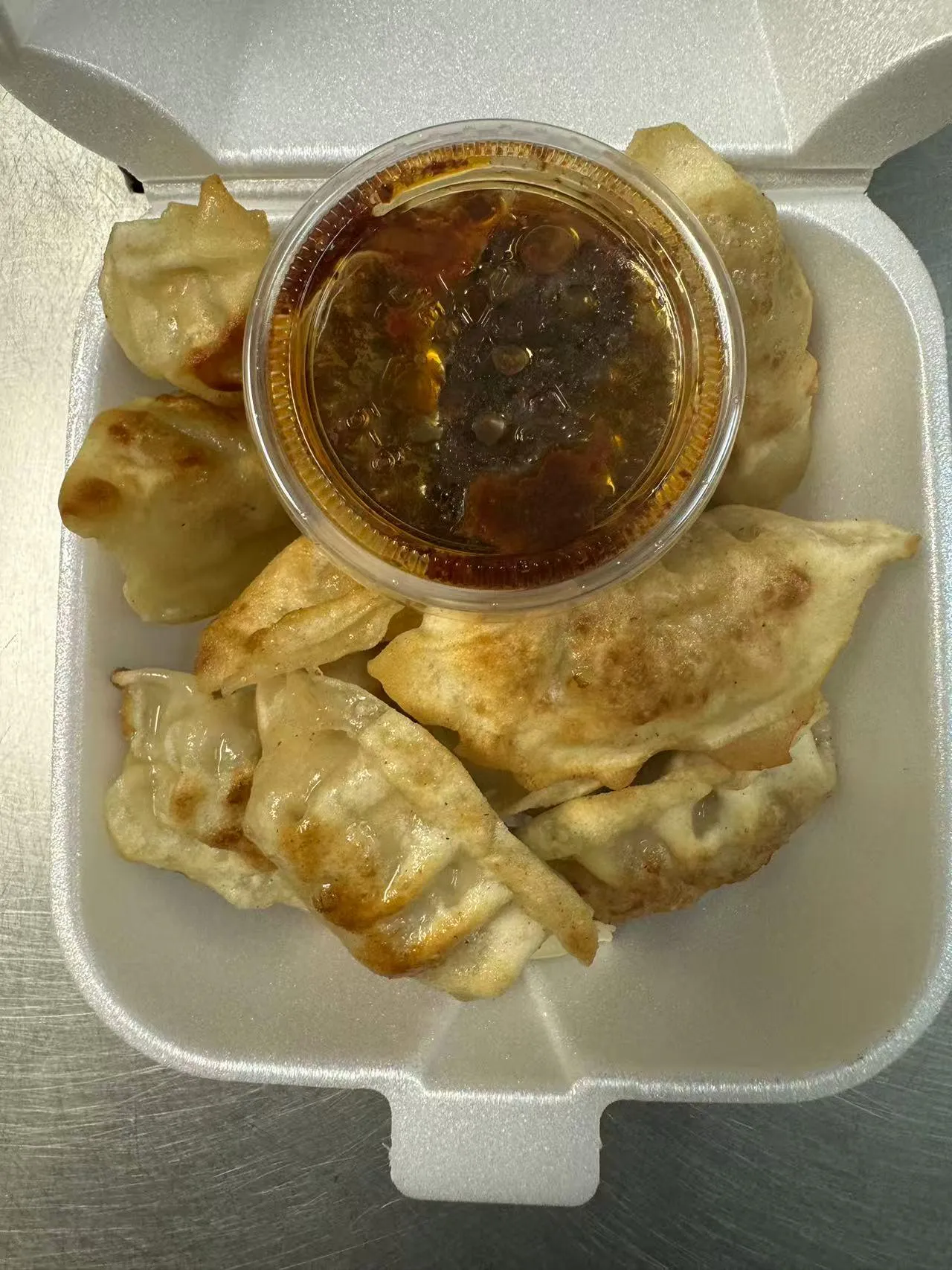 Pan-fried dumplings with a small container of dipping sauce in a takeout box