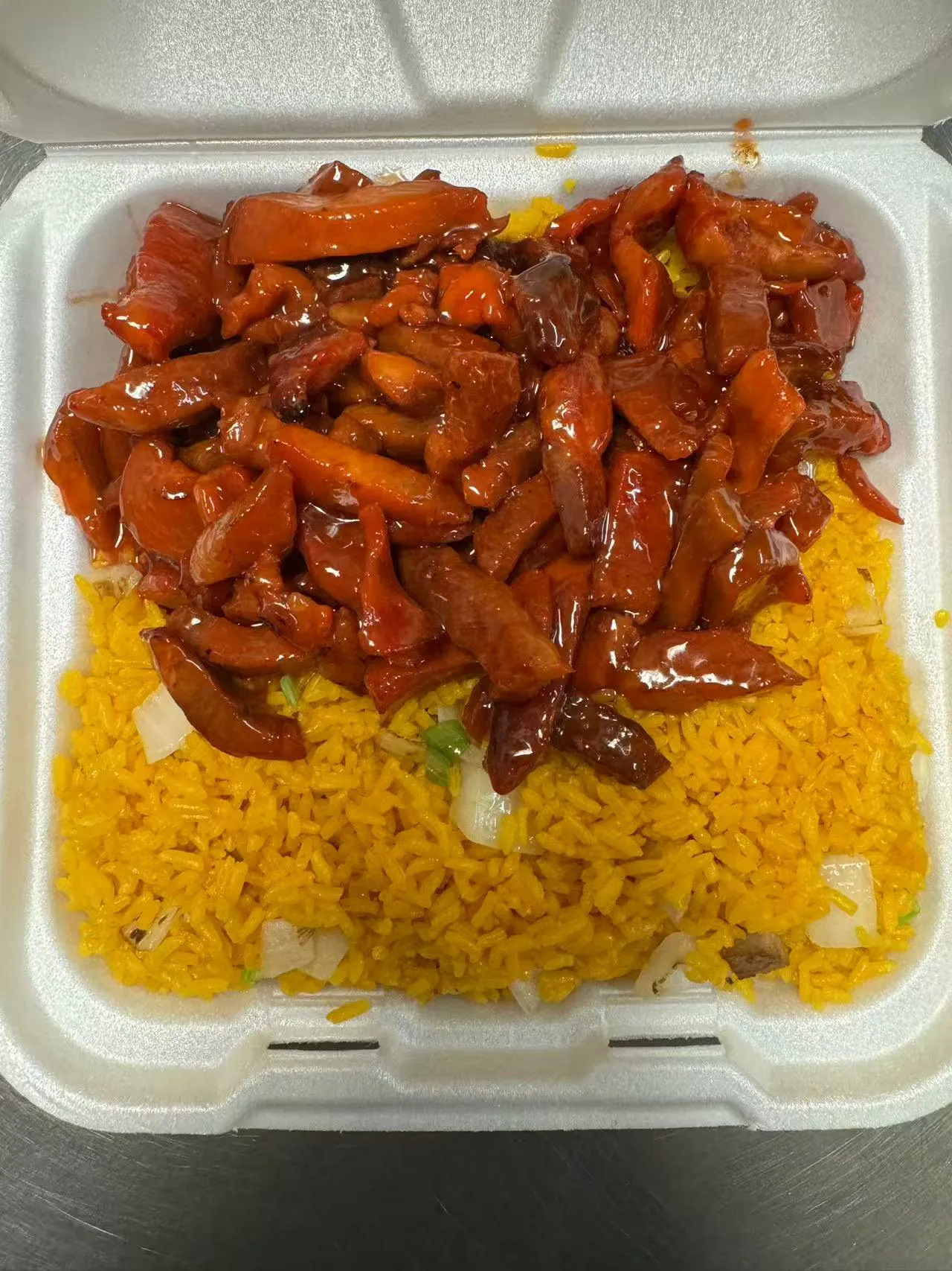 Red glazed meat strips over yellow rice in a takeout box