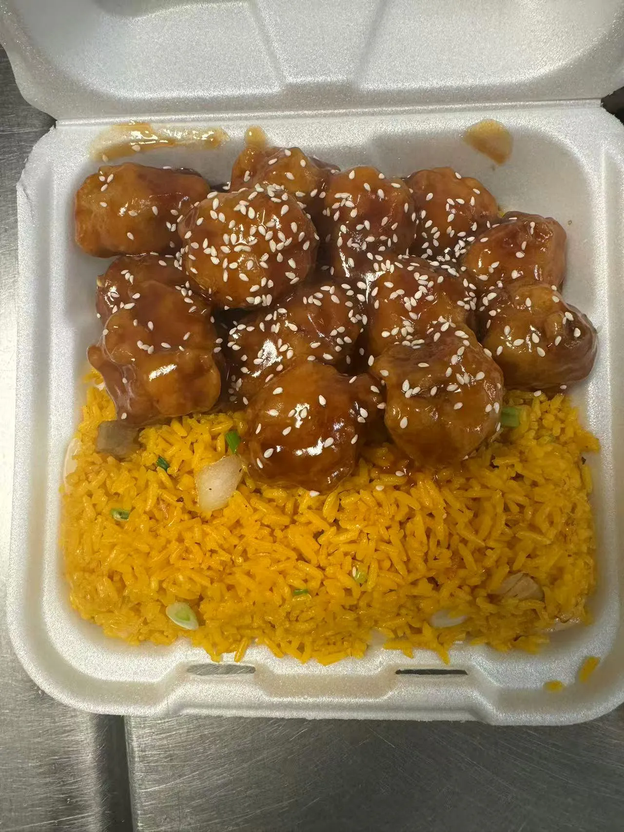 Sesame chicken over yellow rice in a takeout box