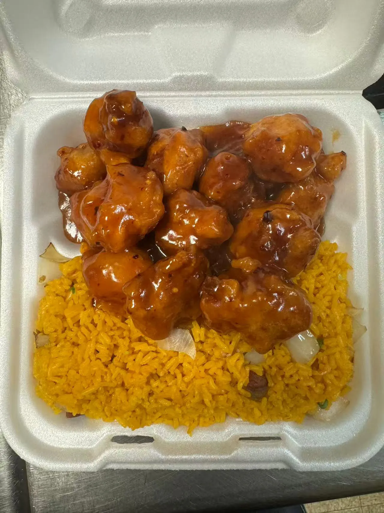 Sweet and sour chicken over yellow rice in a takeout box